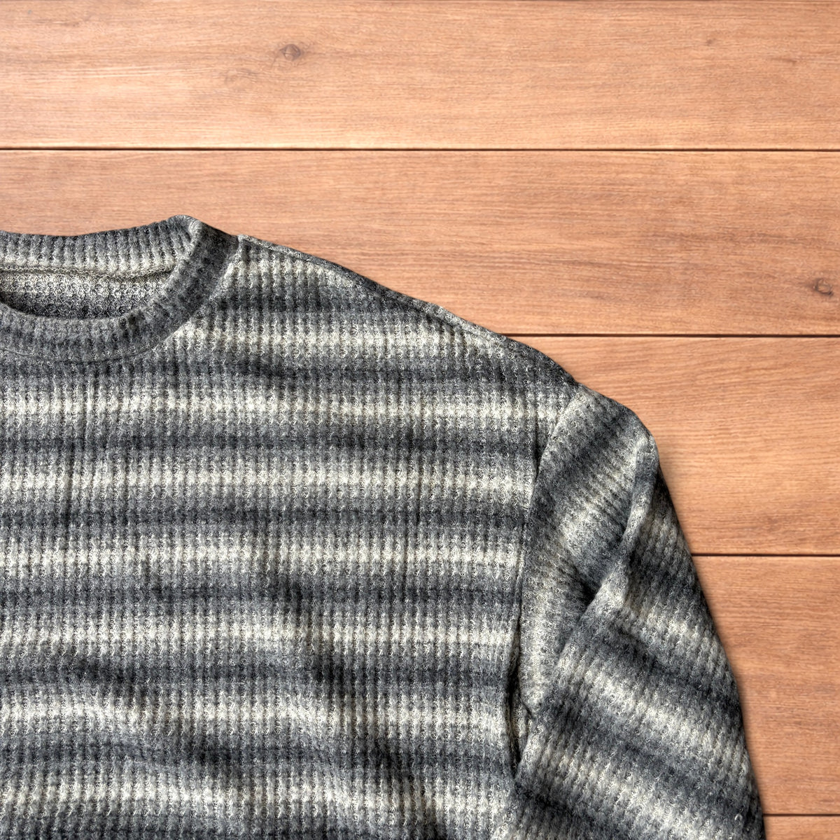 Vintage style knitted sweater jumper with khaki and beige stripes laid flat on wooden surface.