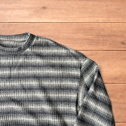 Vintage style knitted sweater jumper with khaki and beige stripes laid flat on wooden surface.