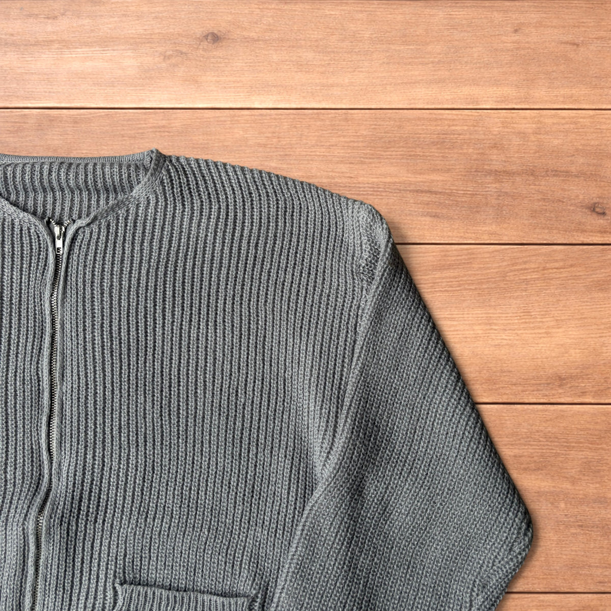 Grey Korean style knitted cardigan jumper with full zip and front pockets laid flat on wooden surface