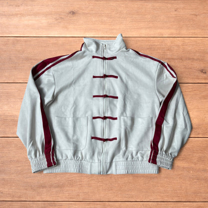 Cream Japanese style zip up track jacket with maroon sleeve stripes and knot button detailing laid flat on wooden surface.