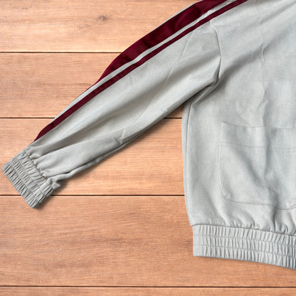 Cream Japanese style zip up track jacket with maroon sleeve stripes and knot button detailing laid flat on wooden surface.