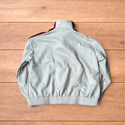 Cream Japanese style zip up track jacket with maroon sleeve stripes and knot button detailing laid flat on wooden surface.