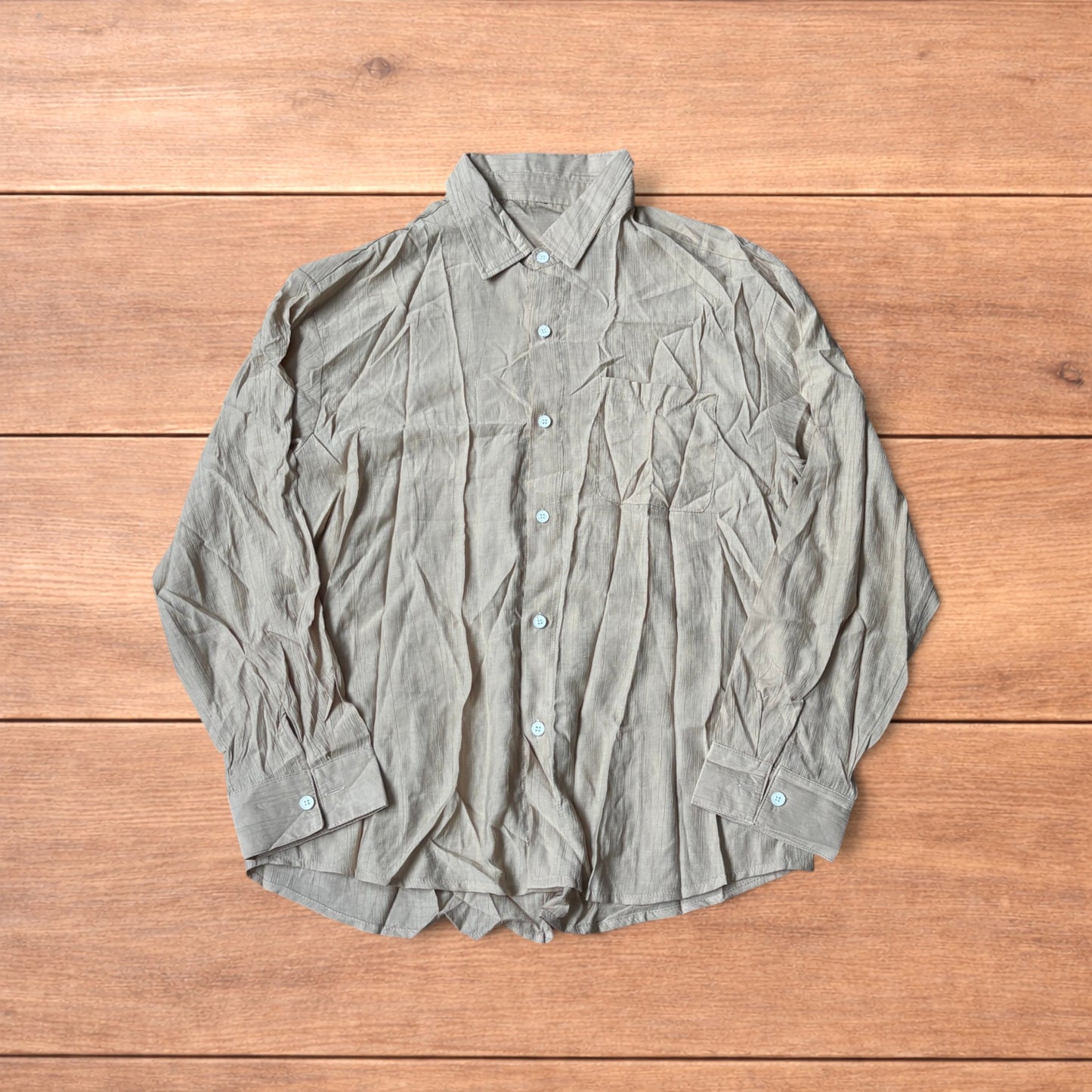 Vintage style camel beige button up long sleeve shirt with light blue buttons and chest pocket laid flat on wooden surface.