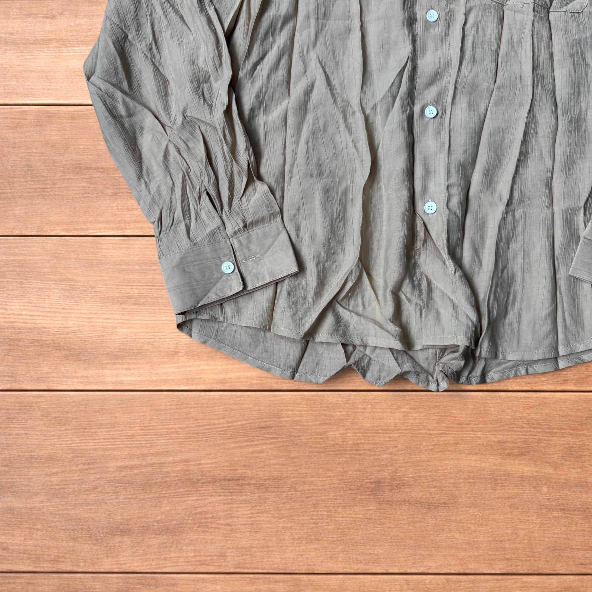 Vintage style camel beige button up long sleeve shirt with light blue buttons and chest pocket laid flat on wooden surface.