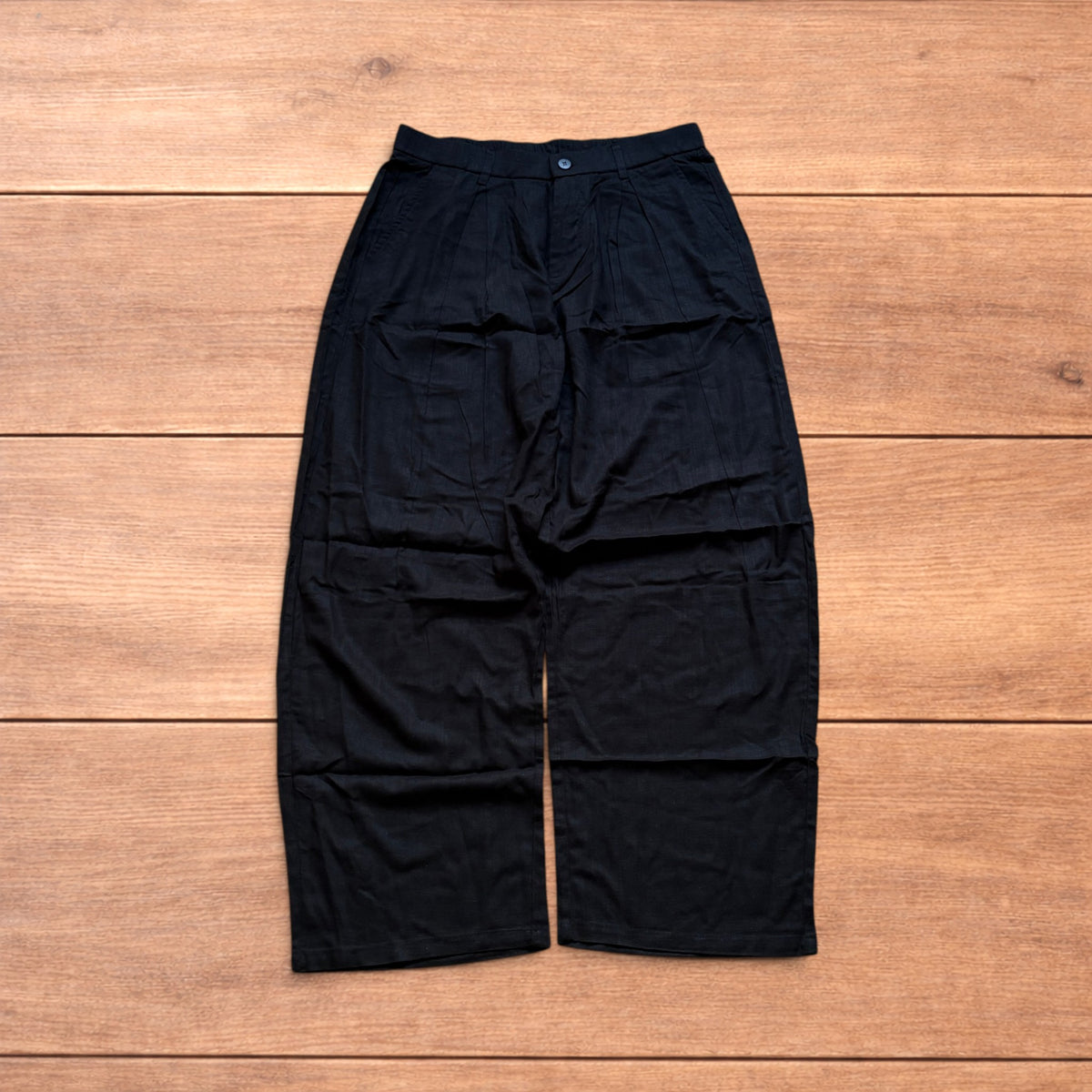 Vintage linen style black baggy wide leg trousers laid flat on wooden background.