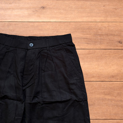 Vintage linen style black baggy wide leg trousers laid flat on wooden background.