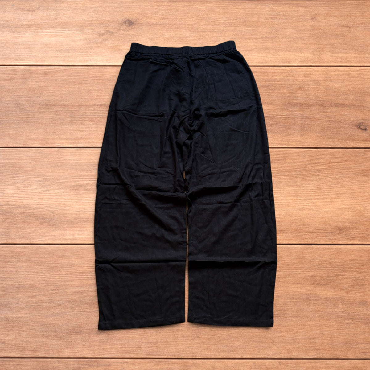Vintage linen style black baggy wide leg trousers laid flat on wooden background.