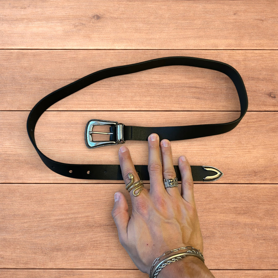 Black vintage style faux leather western cowboy belt with silver buckle and tip on wooden surface