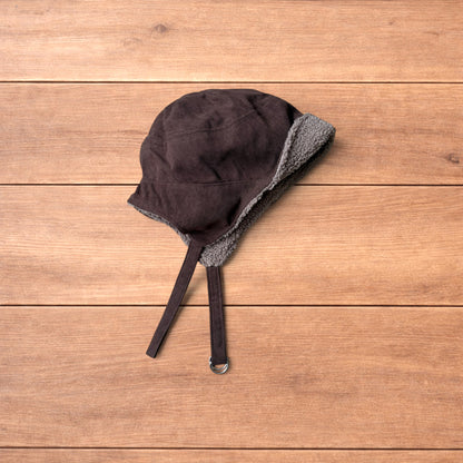 Brown Korean trapper hat with corduroy outer and fluffy woolen lining, laid flat on wooden surface showing ear flaps and chin strap.