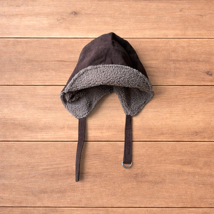 Brown Korean trapper hat with corduroy outer and fluffy woolen lining, laid flat on wooden surface showing ear flaps and chin strap.