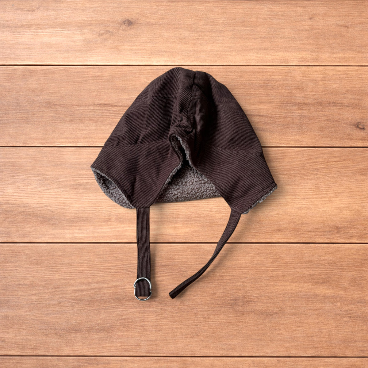 Brown Korean trapper hat with corduroy outer and fluffy woolen lining, laid flat on wooden surface showing ear flaps and chin strap.