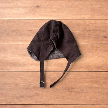 Brown Korean trapper hat with corduroy outer and fluffy woolen lining, laid flat on wooden surface showing ear flaps and chin strap.