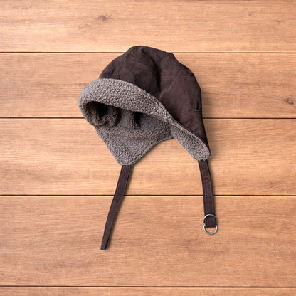 Brown Korean trapper hat with corduroy outer and fluffy woolen lining, laid flat on wooden surface showing ear flaps and chin strap.