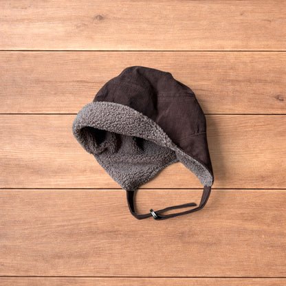 Brown Korean trapper hat with corduroy outer and fluffy woolen lining, laid flat on wooden surface showing ear flaps and chin strap.