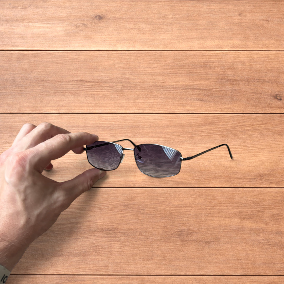 Hand holding vintage style black metal frame sunglasses with purple lenses against a wooden background.
