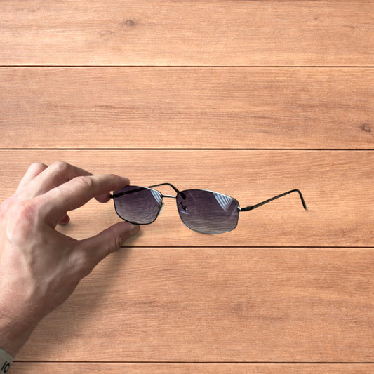 Hand holding vintage style black metal frame sunglasses with purple lenses against a wooden background.