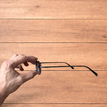 Hand holding vintage style black metal frame sunglasses with purple lenses against a wooden background.