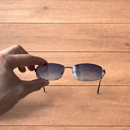 Hand holding vintage style black metal frame sunglasses with purple lenses against a wooden background.