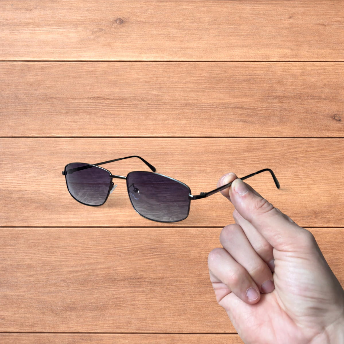 Hand holding vintage style black metal frame sunglasses with purple lenses against a wooden background.