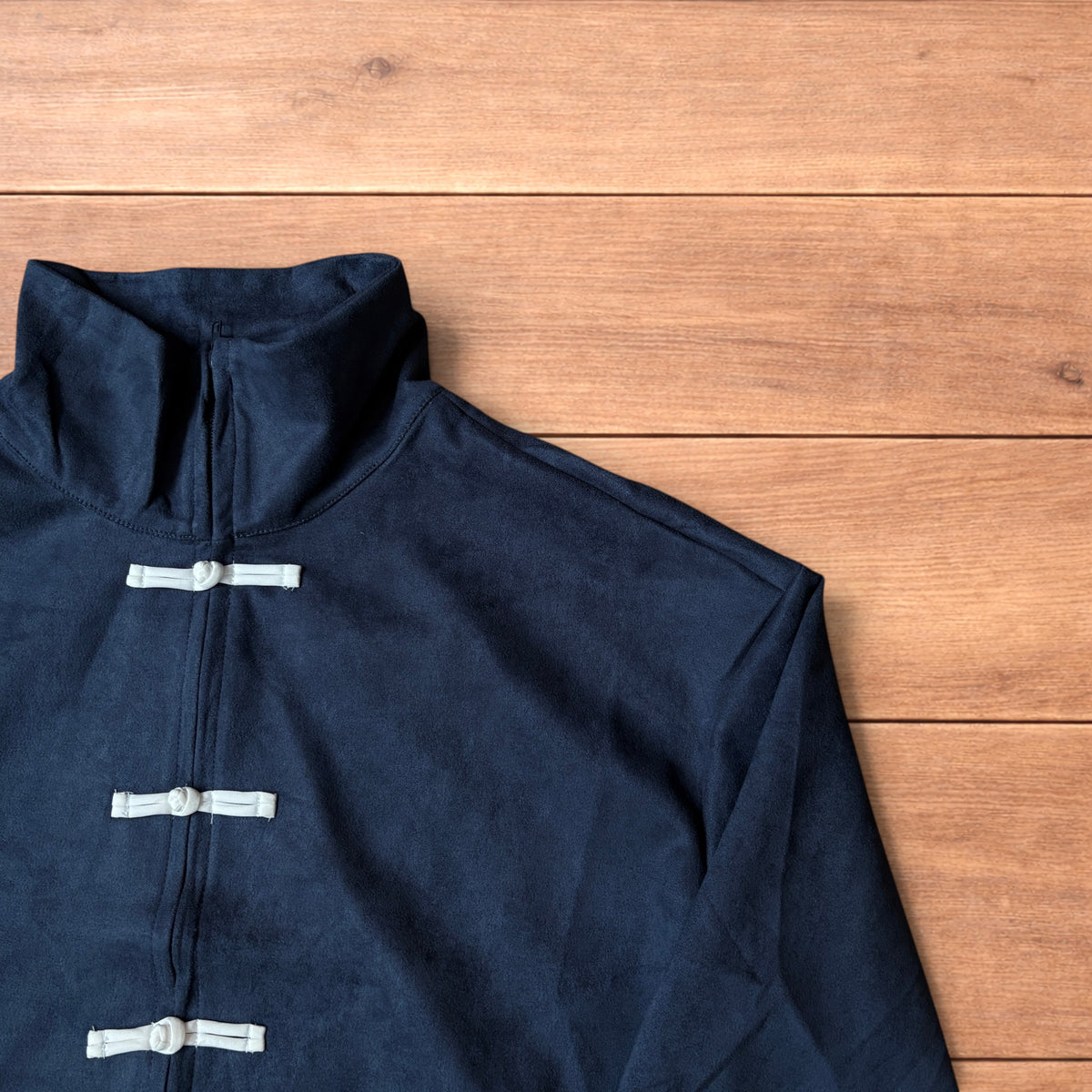 Japanese style navy blue zip up track jacket with white knotted fastenings on wooden background.
