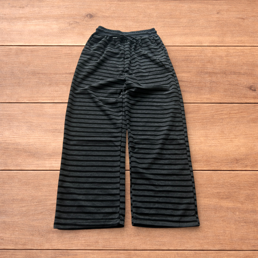Black and grey striped baggy straight leg lounge pants laid flat on wooden surface showing waistband and full length