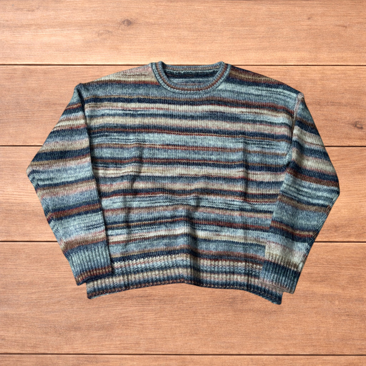 Vintage style striped knitted sweater jumper laid flat on a wooden surface featuring blue and beige marl stripes.