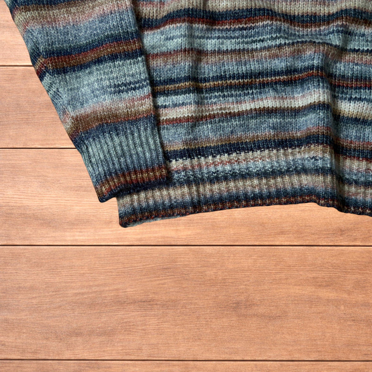 Vintage style striped knitted sweater jumper laid flat on a wooden surface featuring blue and beige marl stripes.