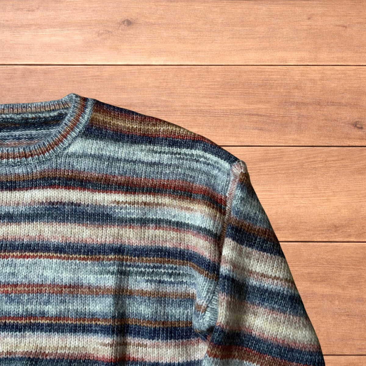 Vintage style striped knitted sweater jumper laid flat on a wooden surface featuring blue and beige marl stripes.