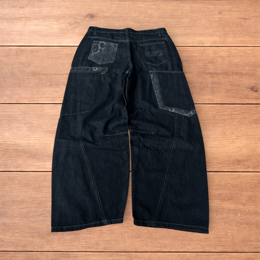 Dark blue vintage style baggy wide leg skater jeans featuring leopard print patches on pockets and hem, laid flat on wooden surface.