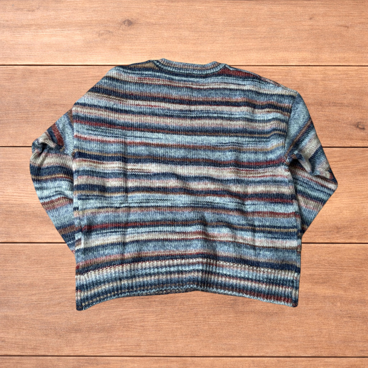 Vintage style striped knitted sweater jumper laid flat on a wooden surface featuring blue and beige marl stripes.