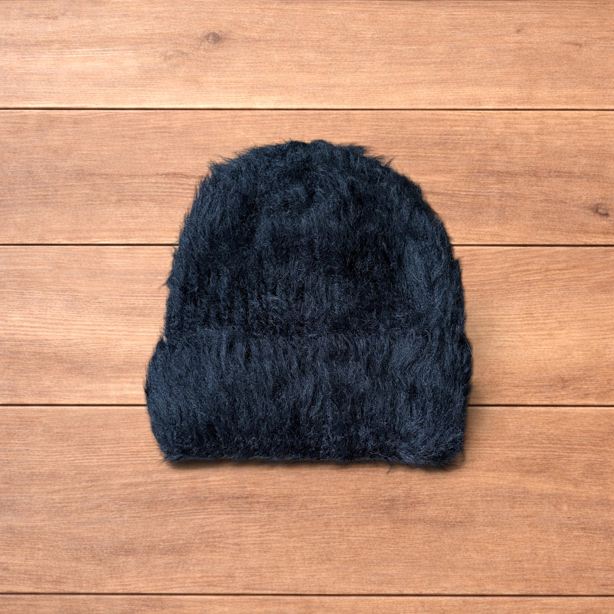Black fluffy beanie with ribbed fold-over cuff on wooden surface.