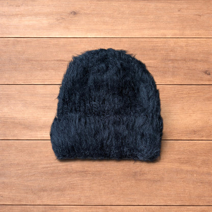Black fluffy beanie with ribbed fold-over cuff on wooden surface.