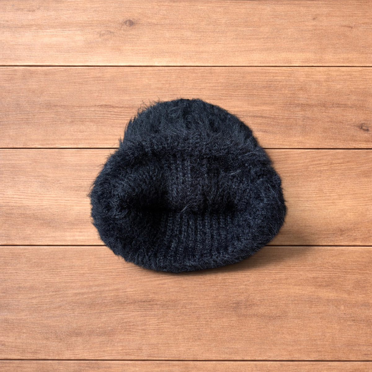 Black fluffy beanie with ribbed fold-over cuff on wooden surface.