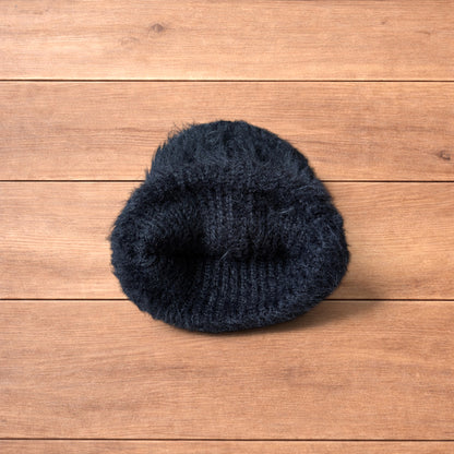 Black fluffy beanie with ribbed fold-over cuff on wooden surface.