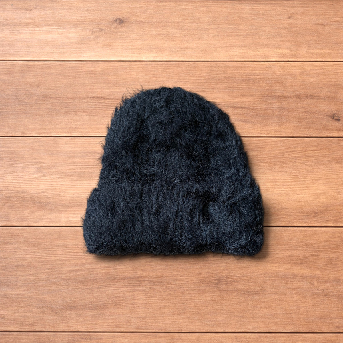 Black fluffy beanie with ribbed fold-over cuff on wooden surface.