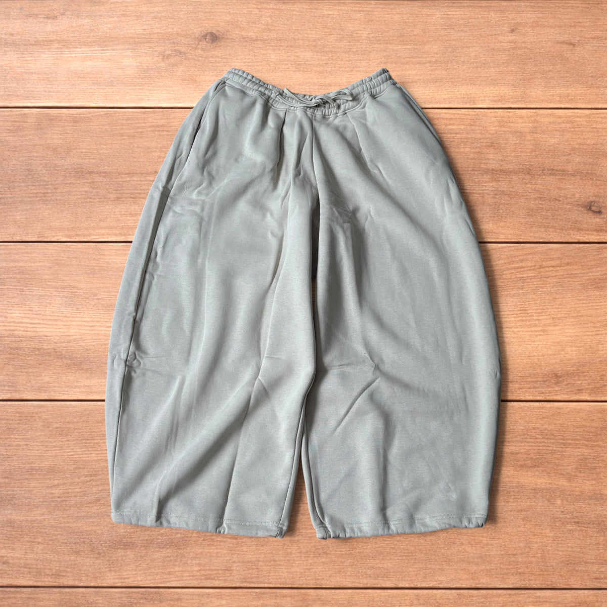 Pale grey baggy joggers laid flat showing elastic waistband with drawstring and wide leg cut.