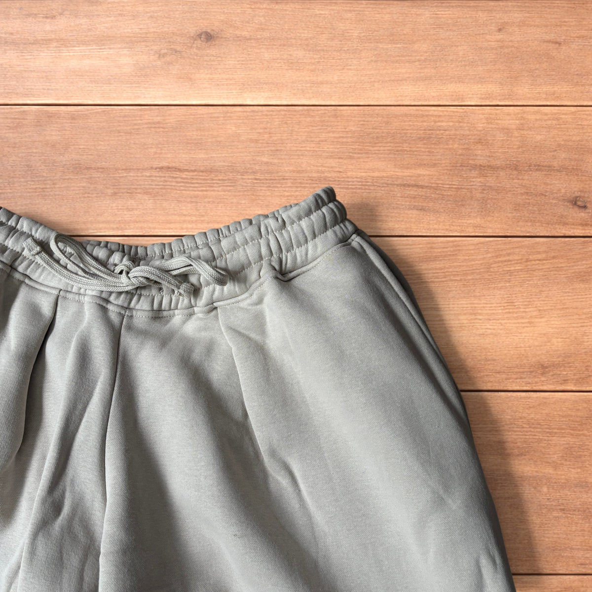 Pale grey baggy joggers laid flat showing elastic waistband with drawstring and wide leg cut.