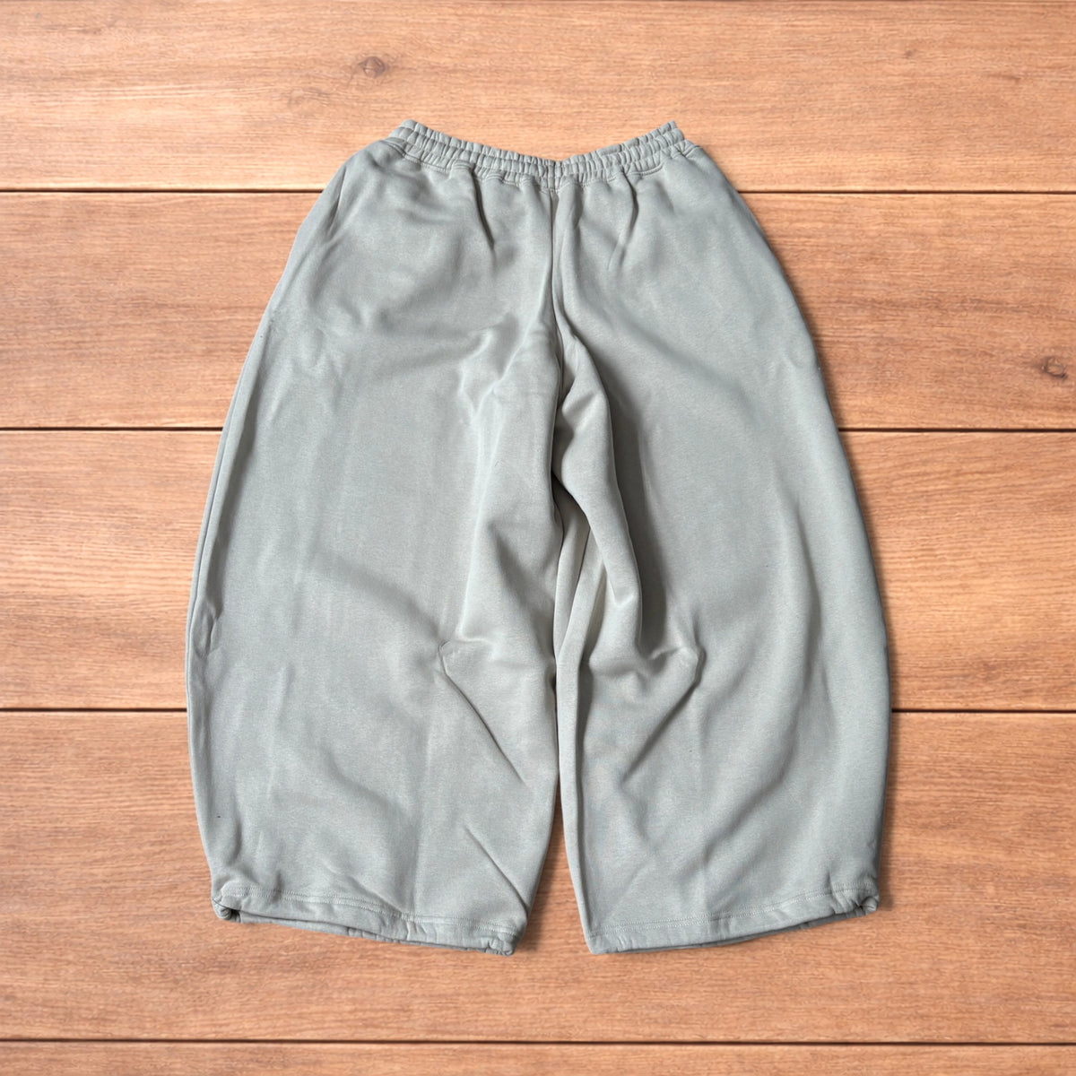 Pale grey baggy joggers laid flat showing elastic waistband with drawstring and wide leg cut.