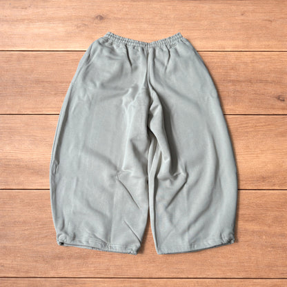 Pale grey baggy joggers laid flat showing elastic waistband with drawstring and wide leg cut.