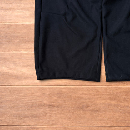 Black baggy wool trousers laid flat on wooden floor showing elasticated waistband and pockets.