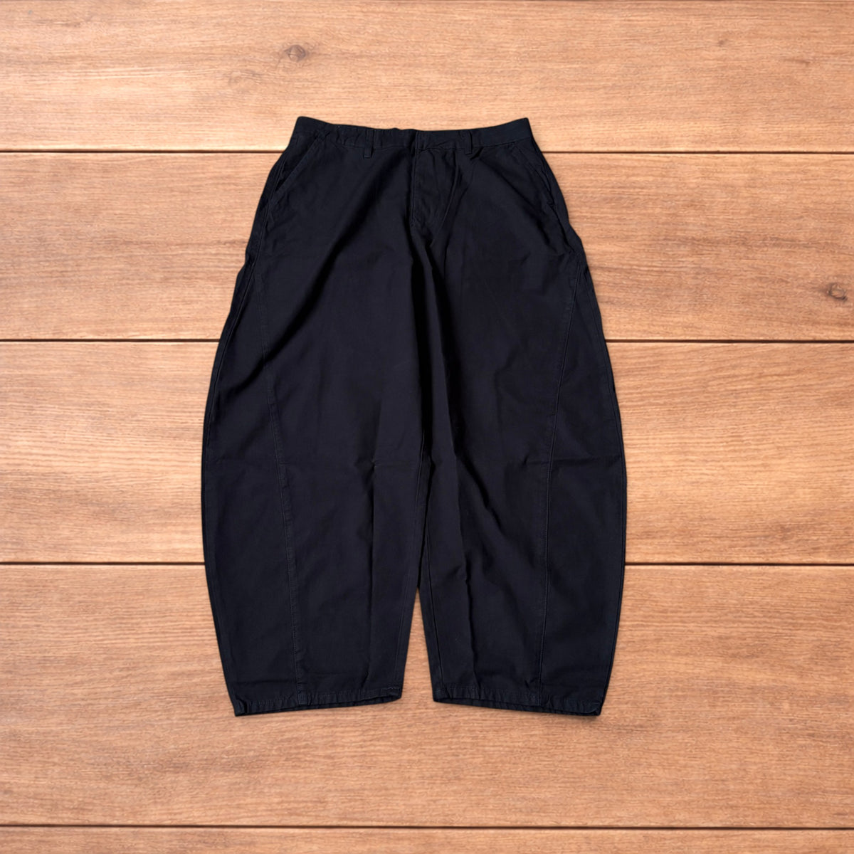 Black baggy balloon chinos laid flat on wooden surface showing wide balloon leg and elasticated hems.