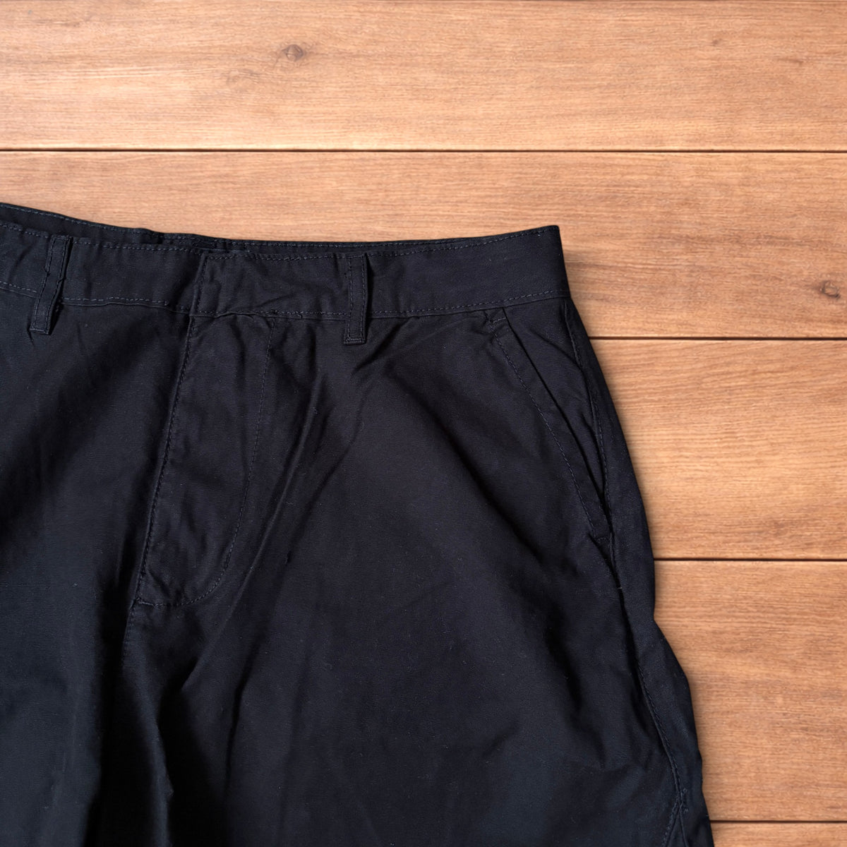 Black baggy balloon chinos laid flat on wooden surface showing wide balloon leg and elasticated hems.