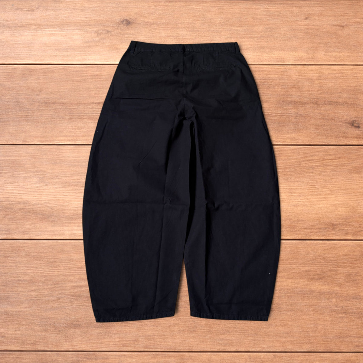 Black baggy balloon chinos laid flat on wooden surface showing wide balloon leg and elasticated hems.