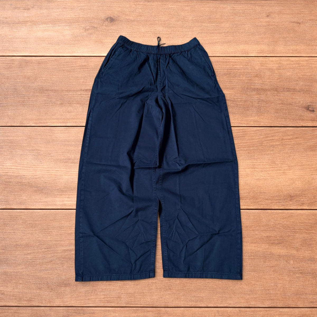 Navy blue baggy chinos laid flat showing elasticated waistband and wide leg cut.