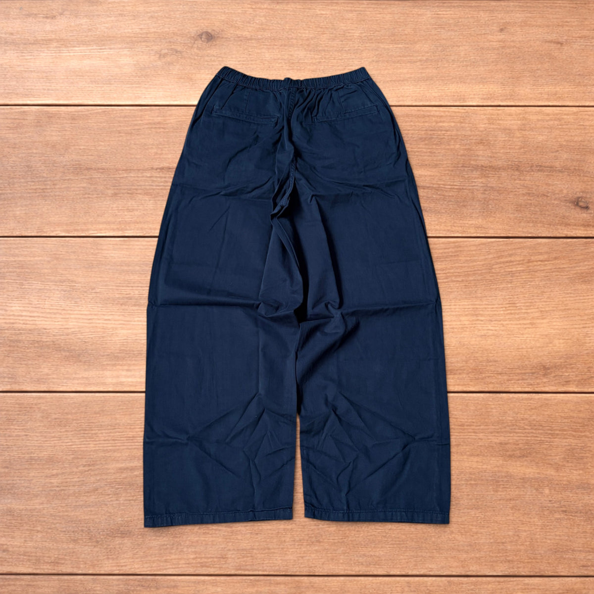 Navy blue baggy chinos laid flat showing elasticated waistband and wide leg cut.