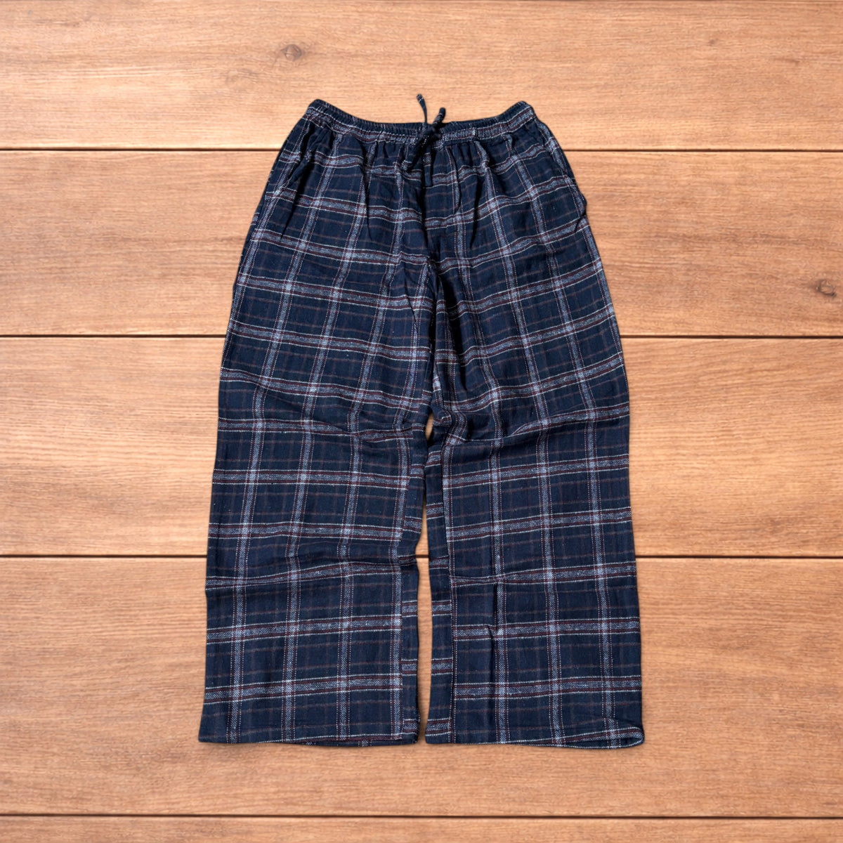 Navy and burgundy plaid baggy loungewear trousers with elasticated waistband and wide legs laid flat on wood surface.