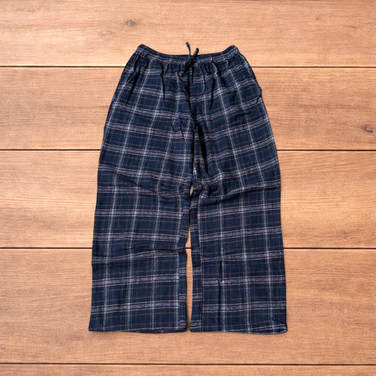 Navy and burgundy plaid baggy loungewear trousers with elasticated waistband and wide legs laid flat on wood surface.