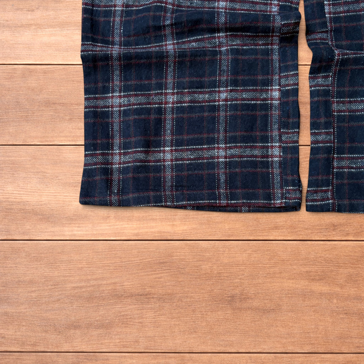 Navy and burgundy plaid baggy loungewear trousers with elasticated waistband and wide legs laid flat on wood surface.