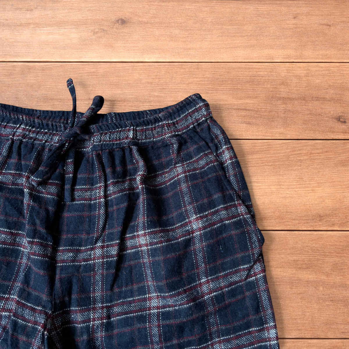 Navy and burgundy plaid baggy loungewear trousers with elasticated waistband and wide legs laid flat on wood surface.