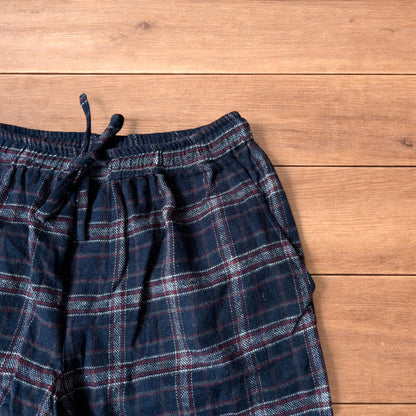Navy and burgundy plaid baggy loungewear trousers with elasticated waistband and wide legs laid flat on wood surface.
